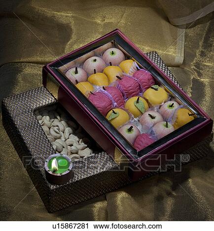 Stock Image - Box of sweets and nuts with a diya. Fotosearch