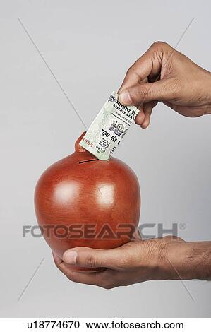 Stock Image - Putting money in a piggy bank. Fotosearch