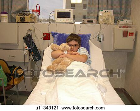 Stock Image - A boy, who has Muscular Dystrophy, hugs his teddy bear before surgery.. Fotosearch