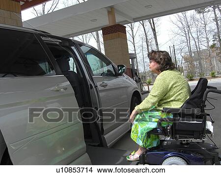 Picture - A woman, who uses a wheelchair, fills her car up with gas.. Fotosearch