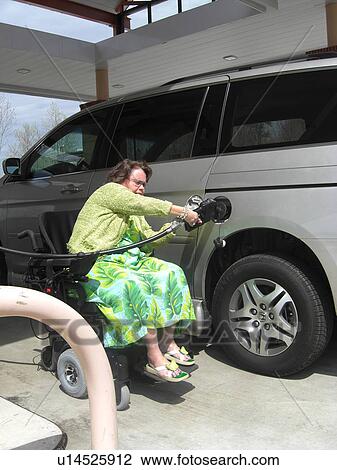 Stock Image - A woman, who uses a wheelchair, fills her car up with gas.. Fotosearch
