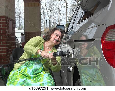 Stock Image - A woman, who uses a wheelchair, fills her car up with gas.. Fotosearch