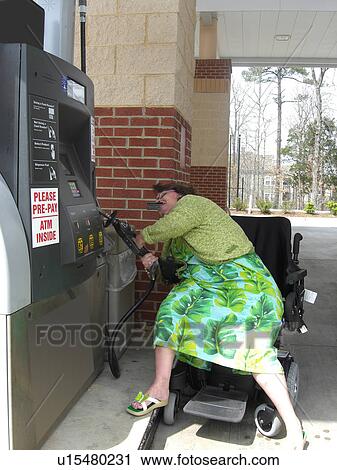 Stock Image - A woman, who uses a wheelchair, fills her car up with gas.. Fotosearch