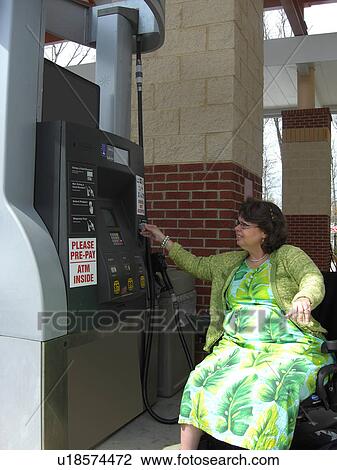 Stock Image - A woman, who uses a wheelchair, fills her car up with gas.. Fotosearch