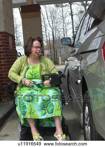 Stock Photo - A woman, who uses a wheelchair, fills her car up with gas.. Fotosearch