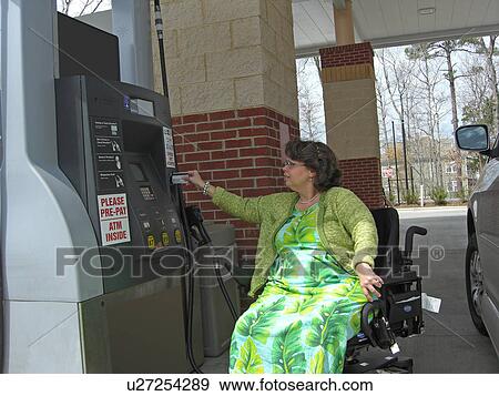 Stock Photo - A woman, who uses a wheelchair, fills her car up with gas.. Fotosearch