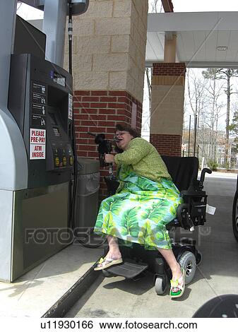 Stock Photograph - A woman, who uses a wheelchair, fills her car up with gas.. Fotosearch