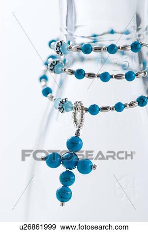 Stock Photo - Blue beaded cross shaped pendant necklace wrapped around a glass jar. Fotosearch