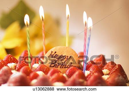Stock Photo - Burning candles on birthday cake, close up. Fotosearch
