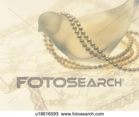 Stock Image - Glass bird figurine, pearl necklace and white lace. Fotosearch