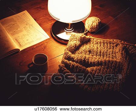 Stock Photograph - Knitting next to pattern book with coffee cup and lamp. Fotosearch
