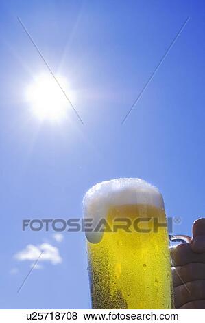 Man holding glass of beer under the sun View Large Photo Image Stock Photo - Man holding glass of beer under the sun. Fotosearch