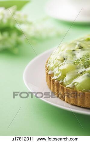 Stock Image - Muscat grape and kiwi tart on plate, green background. Fotosearch