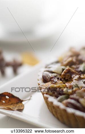 Stock Image - Nut tart and leaf on plate, close up. Fotosearch
