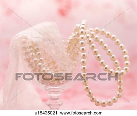 Stock Image - Pearl necklace in a cocktail glass with a pink background. Fotosearch