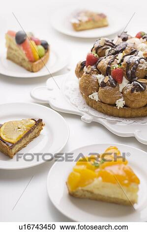Stock Image - Pieces of tart around tart with cream puffs and strawberry, white background. Fotosearch