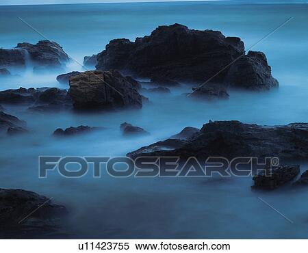 Stock Photography - Rocks in sea rising out of fog. Fotosearch