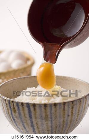 Picture - Row egg being poured on bowl of rice, white background. Fotosearch