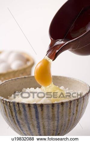 Stock Photo - Row egg being poured on bowl of rice, white background. Fotosearch