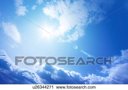 Stock Image - Sun and clouds in blue sky, lens flare. Fotosearch