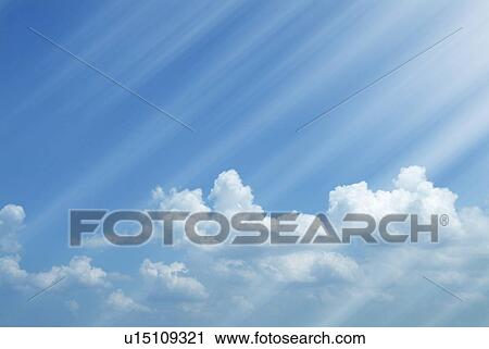 Stock Image - Sunbeams shining on clouds in a blue sky. Fotosearch
