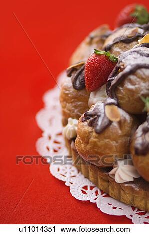Stock Image - Tart with cream puffs and strawberry, close up, red background. Fotosearch