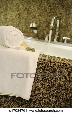 Stock Image - Towels and soaps next to running bath. Fotosearch