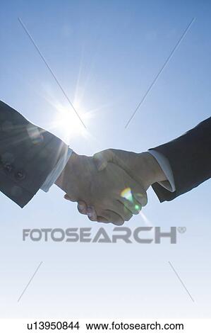 Picture - Two businessmen shaking hands under the sun. Fotosearch