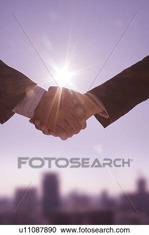 Two businessmen shaking hands under the sun with skyline in background View Large Photo Image Stock Image - Two businessmen shaking hands under the sun with skyline in background. Fotosearch