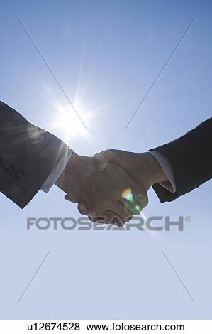 Stock Photo - Two businessmen shaking hands under the sun. Fotosearch