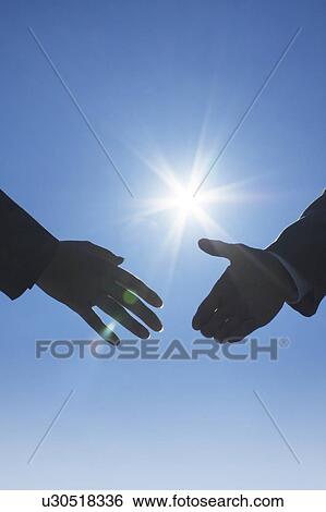 Stock Photograph - Two businessmen shaking hands under the sun. Fotosearch