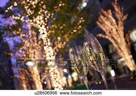 Two champagne glasses toasting on a tree-lined city street decked in fairy lights View Large Photo Image Stock Photograph - Two champagne glasses toasting on a tree-lined city street decked in fairy lights. Fotosearch
