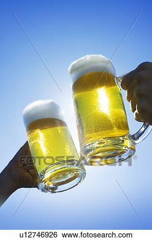 Stock Photograph - Two people toasting glass of beer under the sky. Fotosearch