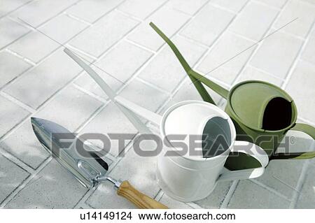 Picture - Watering cans and trowel on a brick patio. Fotosearch