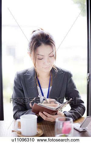 Stock Image - Young businesswoman holding personal organizer in cafe. Fotosearch