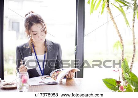 Stock Photo - Young businesswoman reading magazine in cafe. Fotosearch
