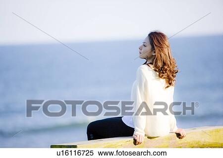 Stock Photography - Young woman sitting on beach, looking away. Fotosearch