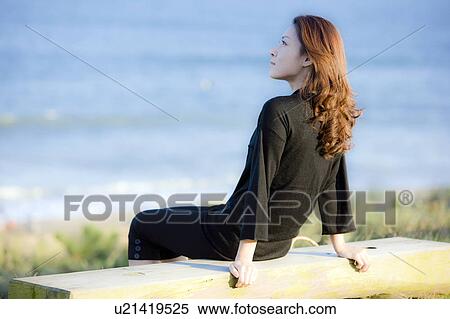 Stock Photography - Young woman sitting on beach, looking away. Fotosearch