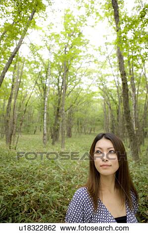 Stock Image - Young woman standing in forest, looking away, Nikko city, Tochigi prefecture, Japan. Fotosearch