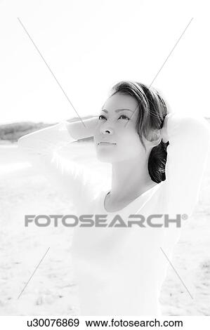 Stock Photo - Young woman standing on beach, looking up. Fotosearch