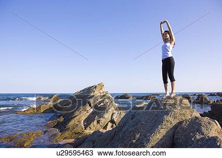 Stock Image - Young woman standing on rock on beach, copy space, Hitachinaka city, Ibaragi prefecture, Japan. Fotosearch