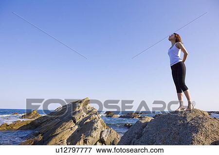 Stock Photo - Young woman standing on rock on beach, copy space, Hitachinaka city, Ibaragi prefecture, Japan. Fotosearch
