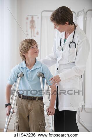 Female doctor assisting boy on crutches View Large Photo Image Stock Photograph - Female doctor assisting boy on crutches. Fotosearch