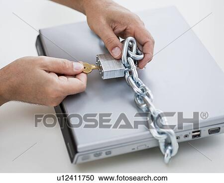 Stock Image - Hands placing lock and chain on computer. Fotosearch