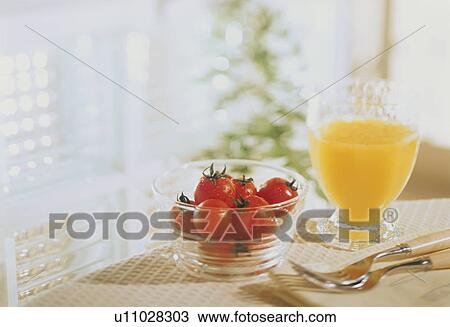 Stock Image - A glass of orange juice and a bowl of cherry tomatoes. Fotosearch