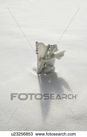 Stock Image - Angel figurine with musical instruments on white sand. Fotosearch