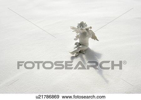 Stock Photo - Angel figurine with musical instruments on white sand. Fotosearch