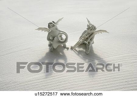 Stock Photo - Angel figurines with musical instruments on white sand. Fotosearch