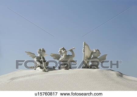 Stock Photo - Angel figurines with musical instruments on white sand. Fotosearch