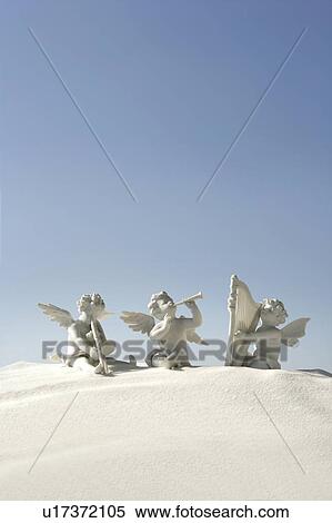 Stock Photography - Angel figurines with musical instruments on white sand. Fotosearch